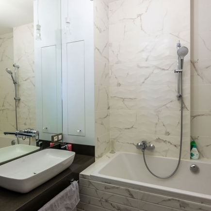 Marble bathroom with soaking tub, handheld shower, and mirrored cabinetry