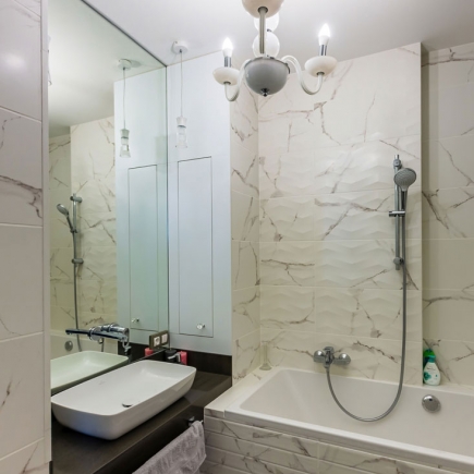Marble-tiled bathroom with vessel sink, mirror, and rainfall shower
