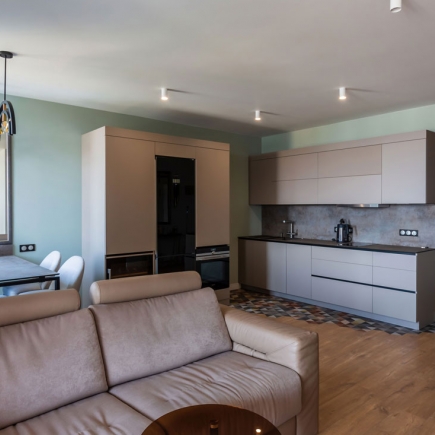 Open-plan kitchen and living room with sage green walls, patterned tile accent floor, and beige leather sofa