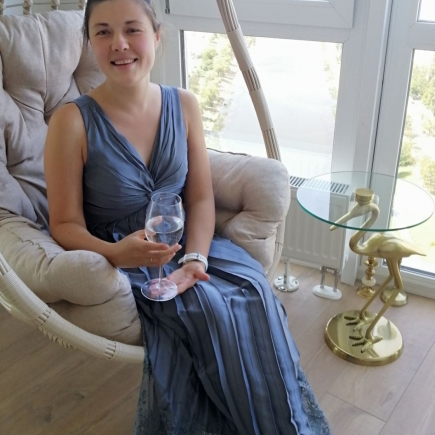 Woman in a blue evening dress relaxing in a rattan swing chair with a glass of wine