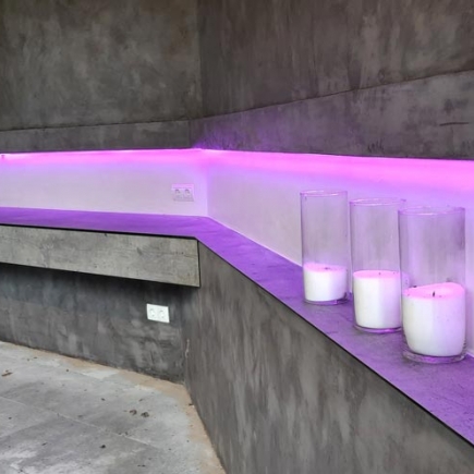Detail of the built-in concrete bench corner lit by a pink LED strip, with pillar candles