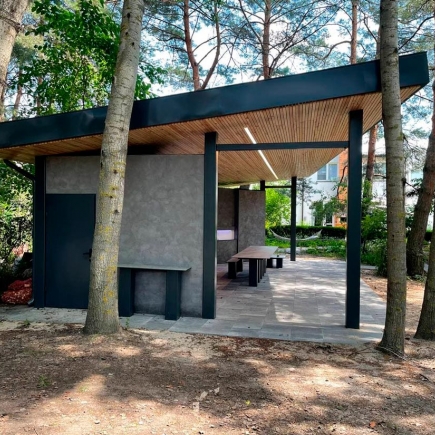 Exterior view of the pavilion nestled among pine trees, with a house visible in the background