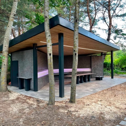Exterior view of the pavilion's cantilevered roof and built-in bench, framed by surrounding pine trees