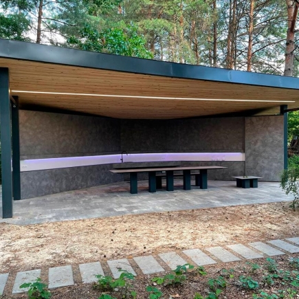 Pavilion interior with concrete walls, integrated sink, and built-in table beneath the wood-slat roof