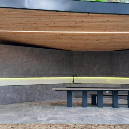 Pavilion interior with concrete walls, integrated sink lit by amber LED strip, and built-in table