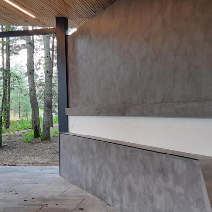 Pavilion support column and concrete wall detail with a wooded path visible beyond