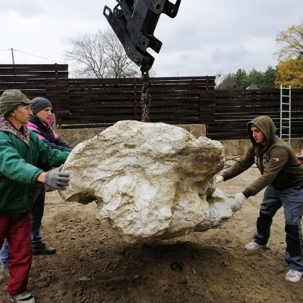 Crew using a crane arm to lift a large decorative boulder into place