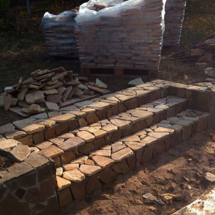 Flagstone garden steps under construction beside stacked stone pallets