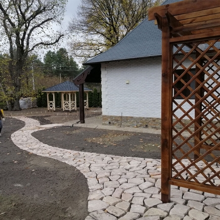 Stone pathway construction beside the cottage with a pergola frame taking shape nearby