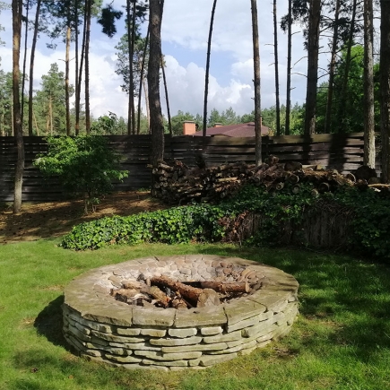 Stone-ringed fire pit set on the lawn among tall pines