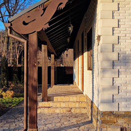 White brick cottage with dark slate roof, twin dormer windows, and paired wood-paneled entry doors