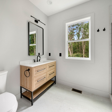 Bathroom vanity in light wood with round mirror and window view of the trees