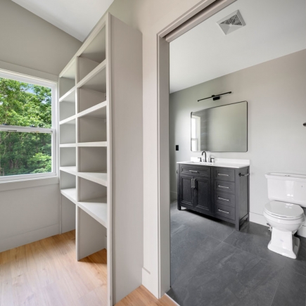 Built-in shelving beside a bedroom window opening into a bathroom with dark vanity