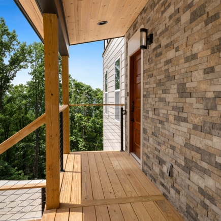 Covered front porch with wood ceiling, stone accent wall, and front door