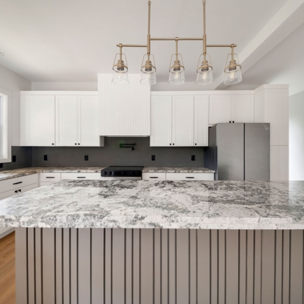 Kitchen island with marble countertop, brass pendant lighting, and stainless refrigerator