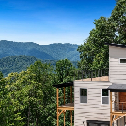 Modern Mountain Living — exterior view from the hillside with mountain ridgeline behind the home