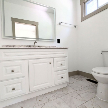Bathroom vanity with framed mirror and marble-look countertop beside the toilet