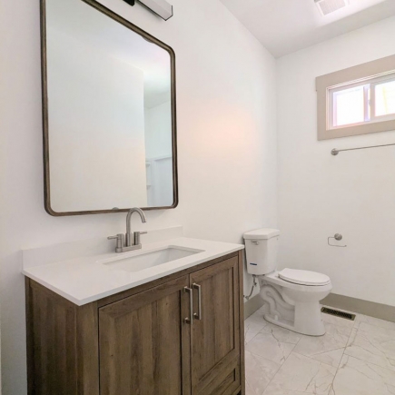 Bathroom with wood vanity, framed mirror, toilet, and marble-tiled floor