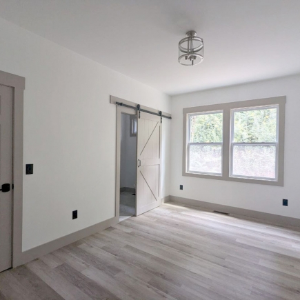 Bedroom with sliding barn door to the bathroom and double window with wooded view