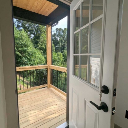 Glass-paneled side door opening onto the covered porch with wooded view