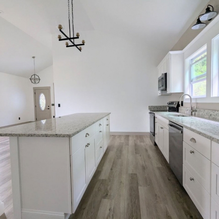 Kitchen galley view with granite island, stainless appliances, and front door beyond