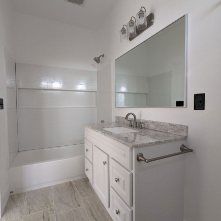 Bathroom with tiled tub-shower combo, white vanity, and lighted mirror