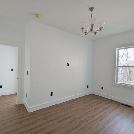 Bedroom corner with chandelier and window, hallway visible through the doorway