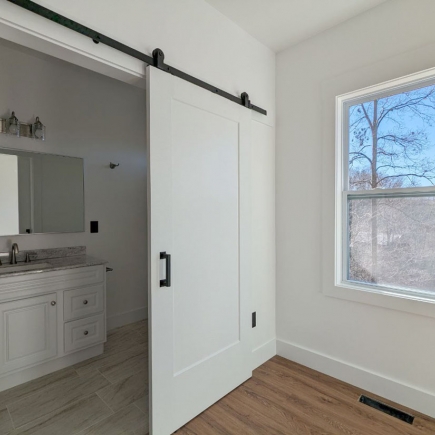 Bedroom with sliding barn door open to an en-suite bathroom and a window view of bare trees