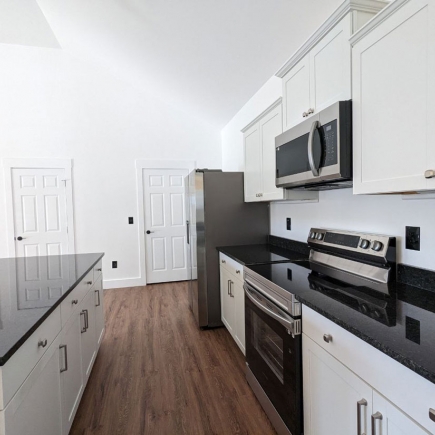 Galley kitchen view with white cabinetry, dark countertops, and stainless range