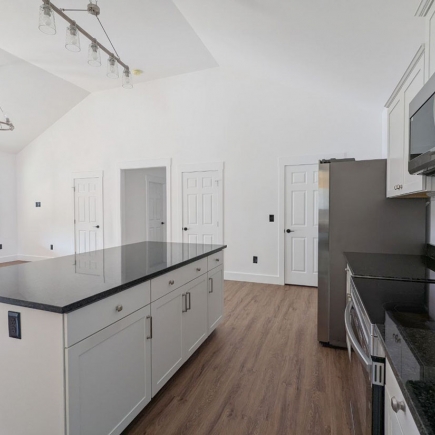 Kitchen island with dark countertop and stainless refrigerator under a vaulted ceiling