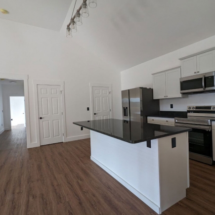 Kitchen island with dark countertop, stainless refrigerator, and hallway to bedrooms beyond