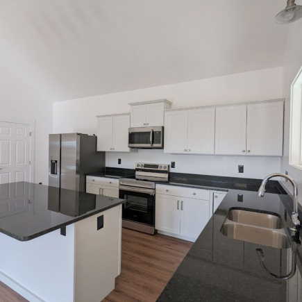 Kitchen with white cabinetry, stainless appliances, and dark countertops under a vaulted ceiling