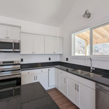 L-shaped kitchen with dark countertops, stainless appliances, and window over the sink