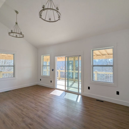 Living room with vaulted ceiling, dual chandeliers, and sliding glass door framed by windows