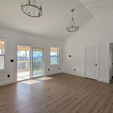 Living room with vaulted ceiling, twin chandeliers, and sliding door to the deck