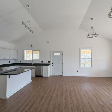 Open-concept kitchen and living area with vaulted ceiling and dual chandeliers