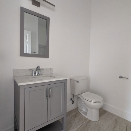 Powder room with gray vanity, framed mirror, and toilet