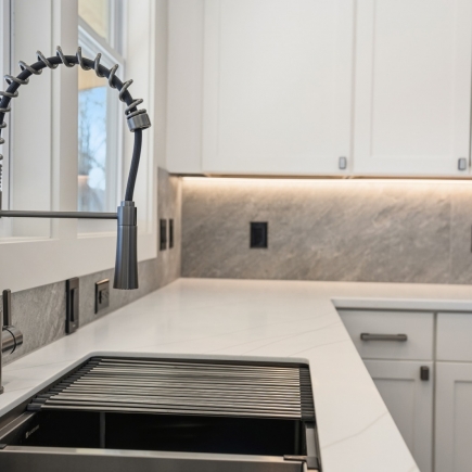 Kitchen sink and pull-down faucet detail with marble countertop and backsplash